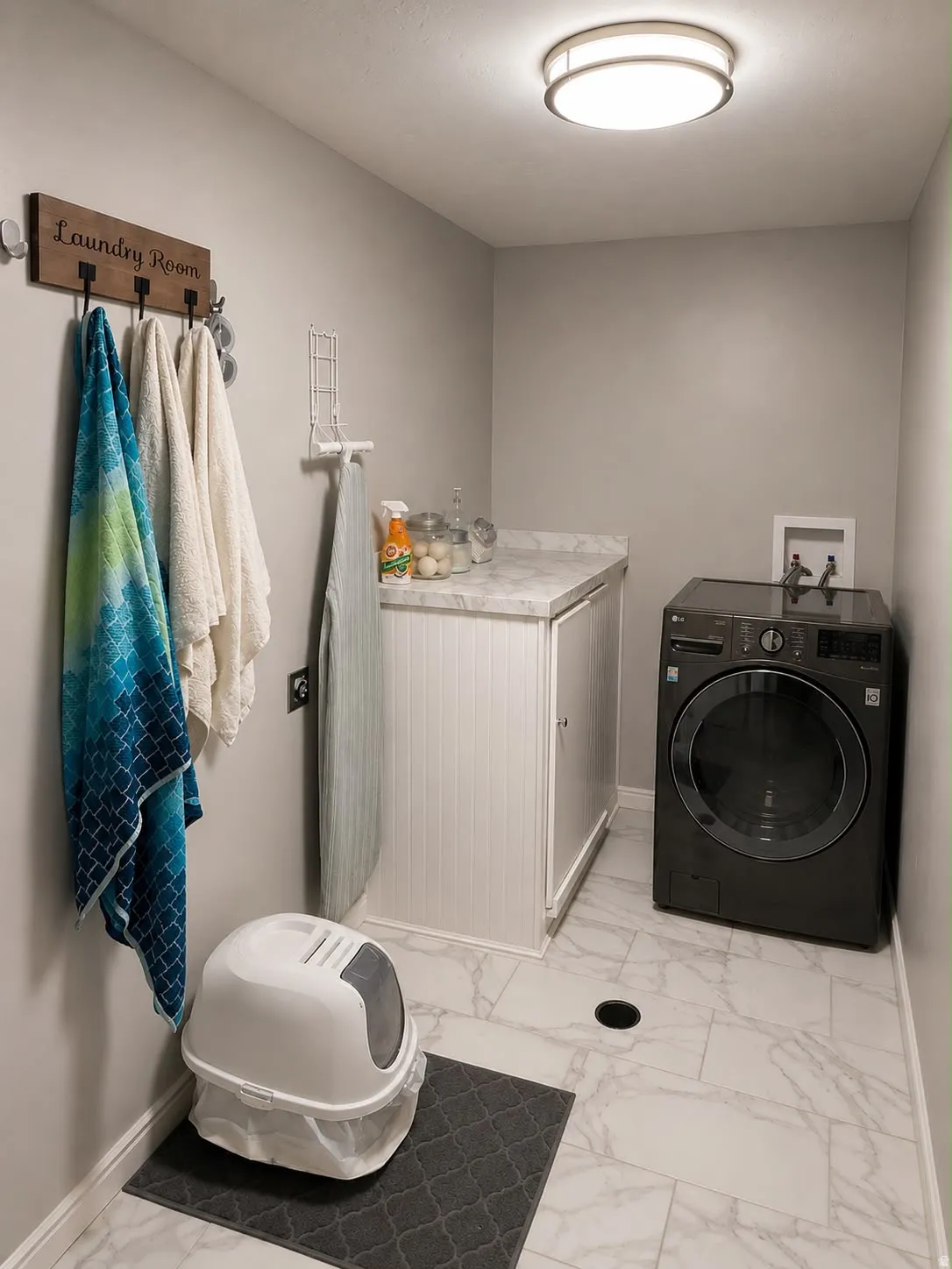 Laundry area featuring white marble-look tile flooring, gray walls, built-in cabinetry with a white countertop, and flush-mount ceiling lighting