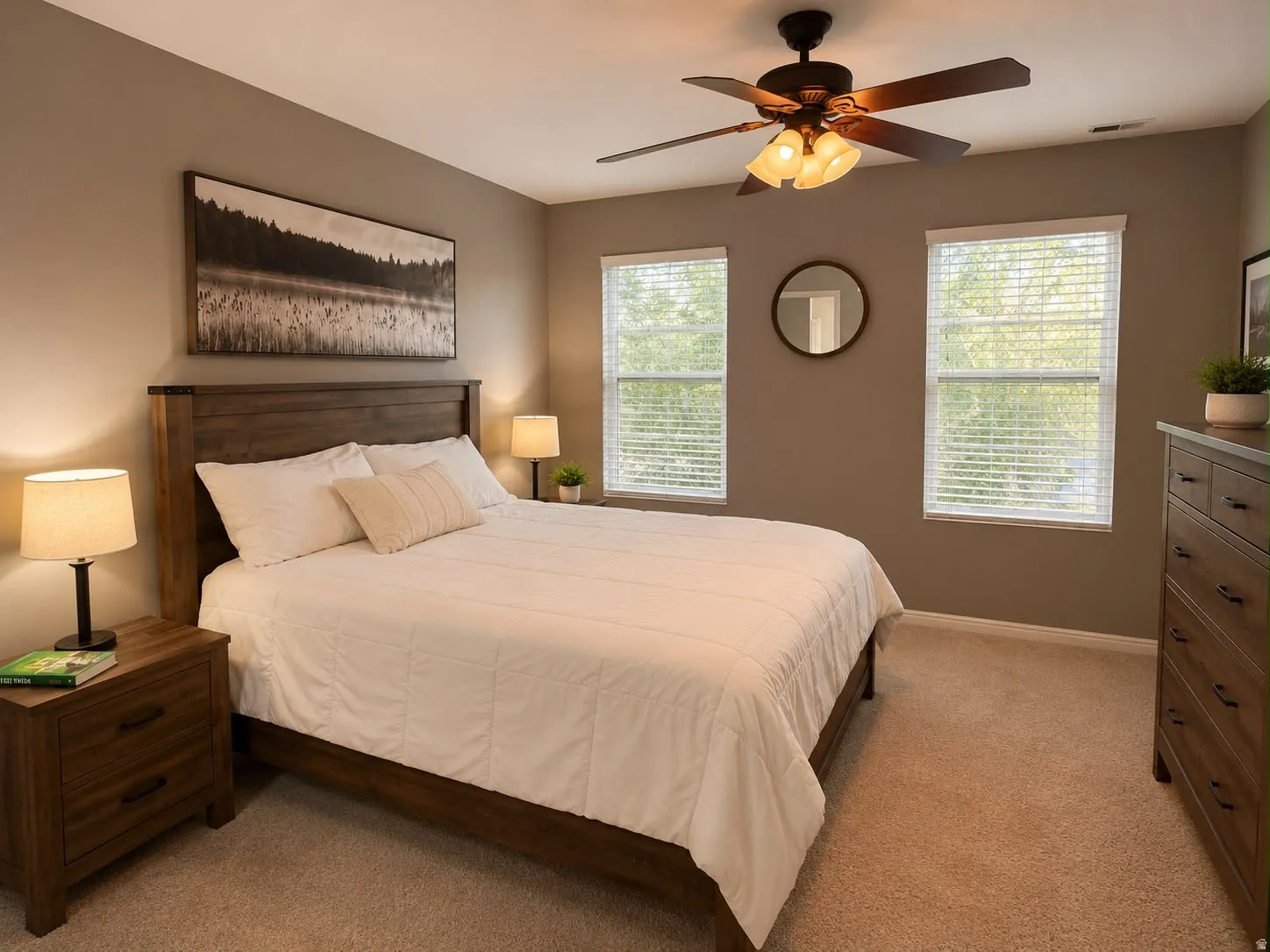 Carpeted room featuring a wood-finish bed frame, two windows with blinds, a ceiling fan with integrated lighting, and a wood-finish dresser