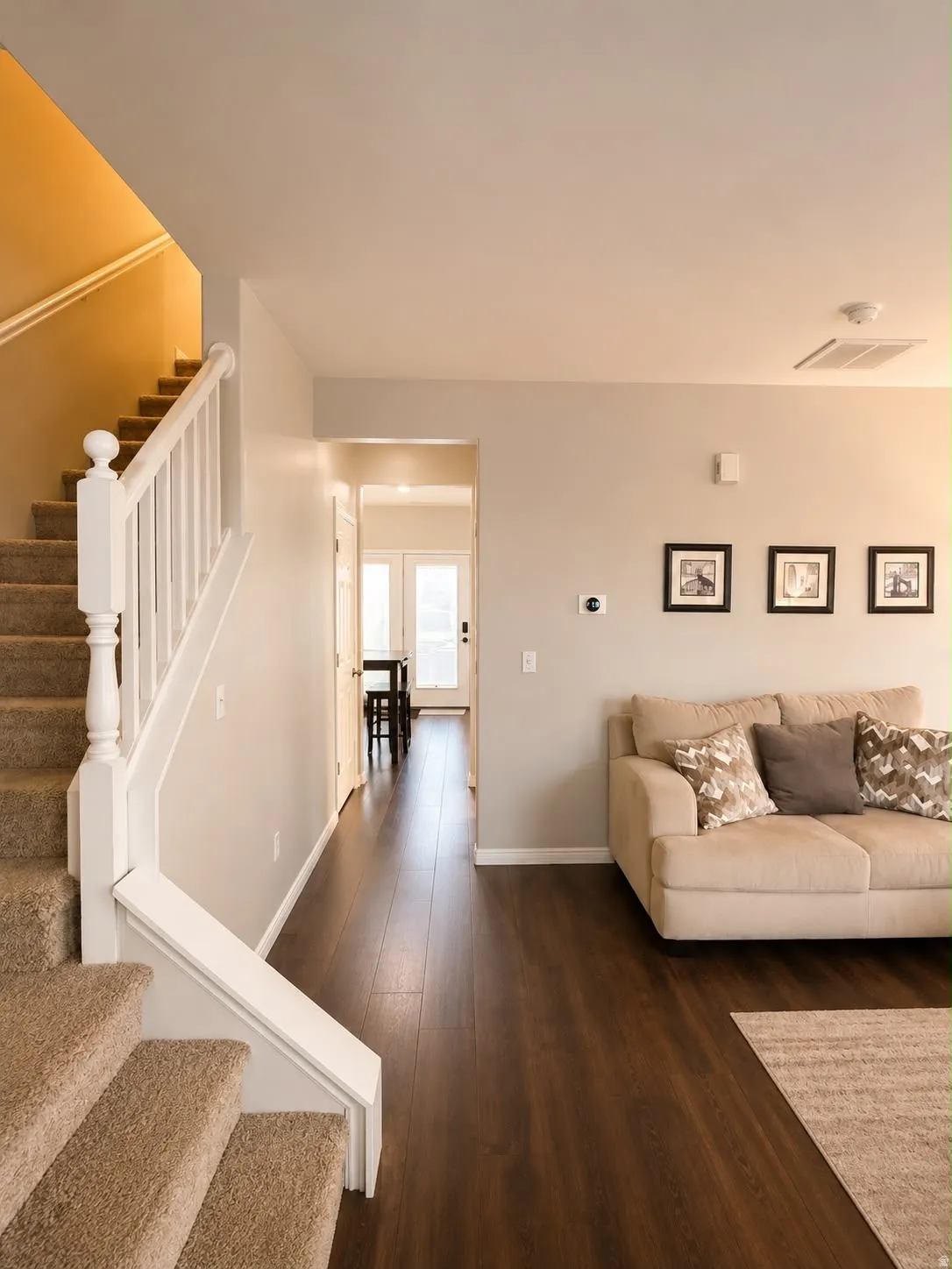 Hallway featuring wood-finish flooring, a carpeted staircase with white balusters, and light-toned walls