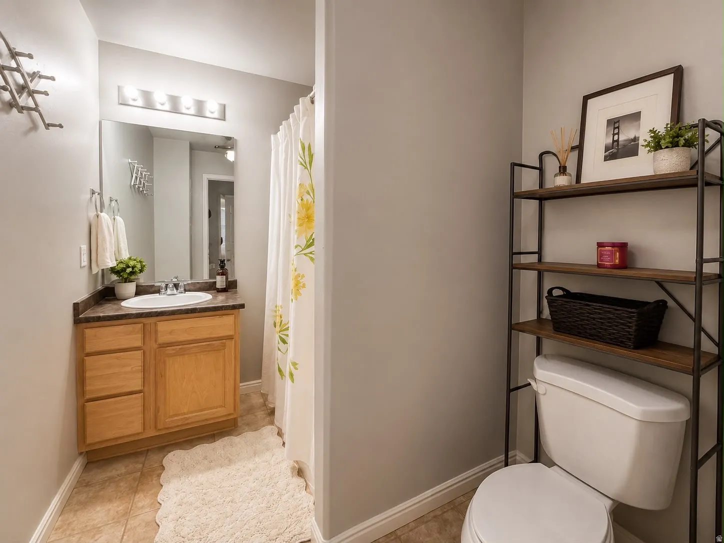 Bathroom featuring a wood-finish vanity with a built-in sink and dark countertop, an overhead mirror with vanity lighting, and tile flooring