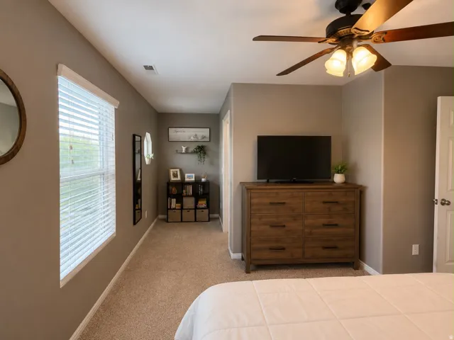 Carpeted room featuring a ceiling fan with integrated lighting, a window with blinds, and a built-in shelf unit