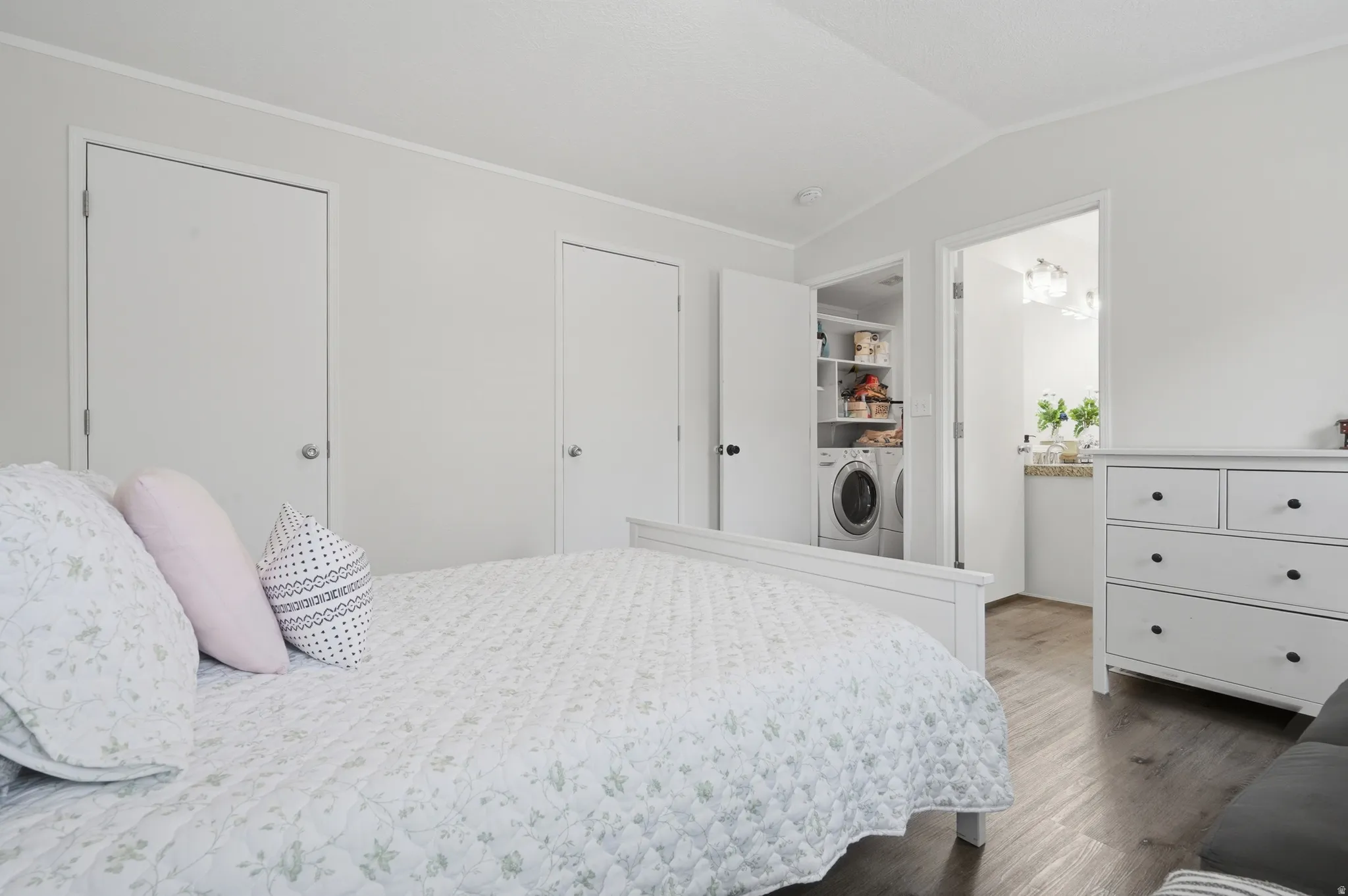 Bedroom featuring white walls, wood-finish flooring, and an open doorway to an adjacent laundry closet with built-in shelving