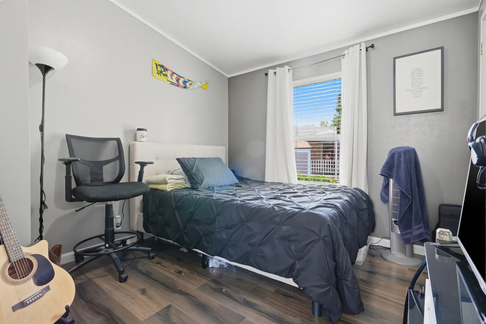 Spacious room featuring wood-finish flooring, light grey painted walls, and a large window with white blinds