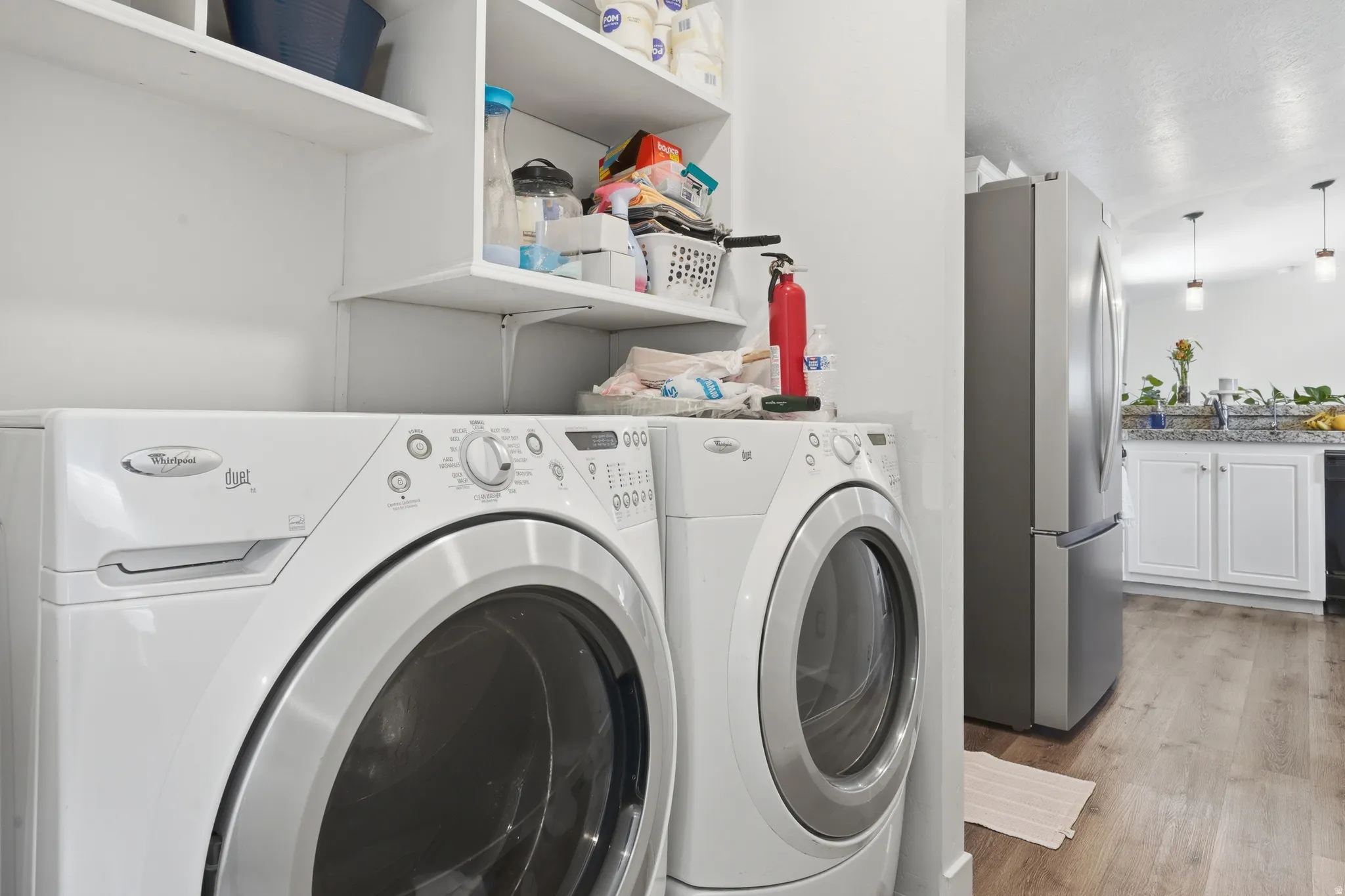 Functional laundry area featuring built-in shelving, white appliances, and wood-finish flooring