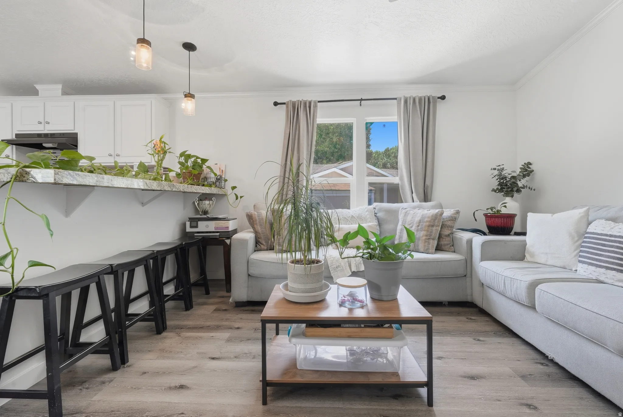 Open-concept living area featuring wood-finish flooring, white cabinetry, a breakfast bar with a stone-finish countertop, and pendant lighting