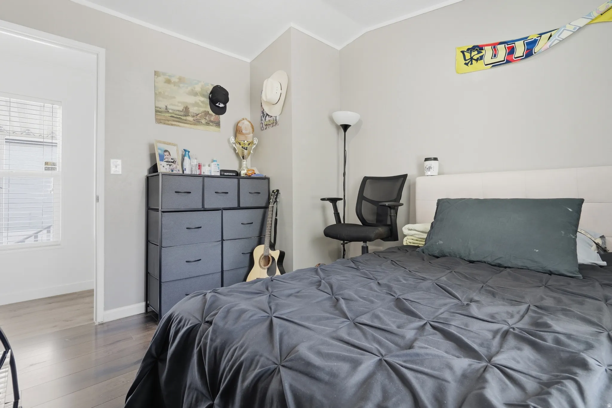 Bedroom featuring dark wood-finish flooring, light grey painted walls, white baseboards, and a white interior door frame