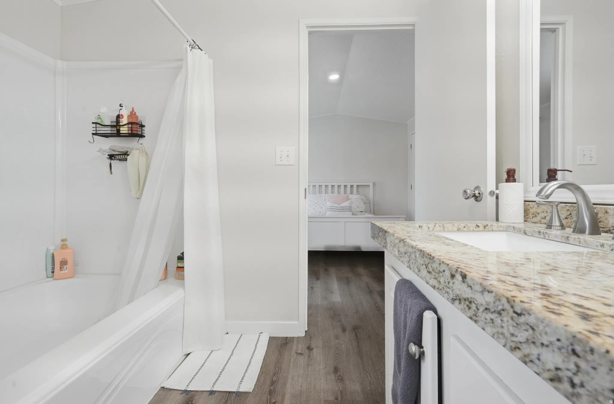 Bathroom featuring a white bathtub, shower with white surround, and a vanity with a light-toned granite countertop