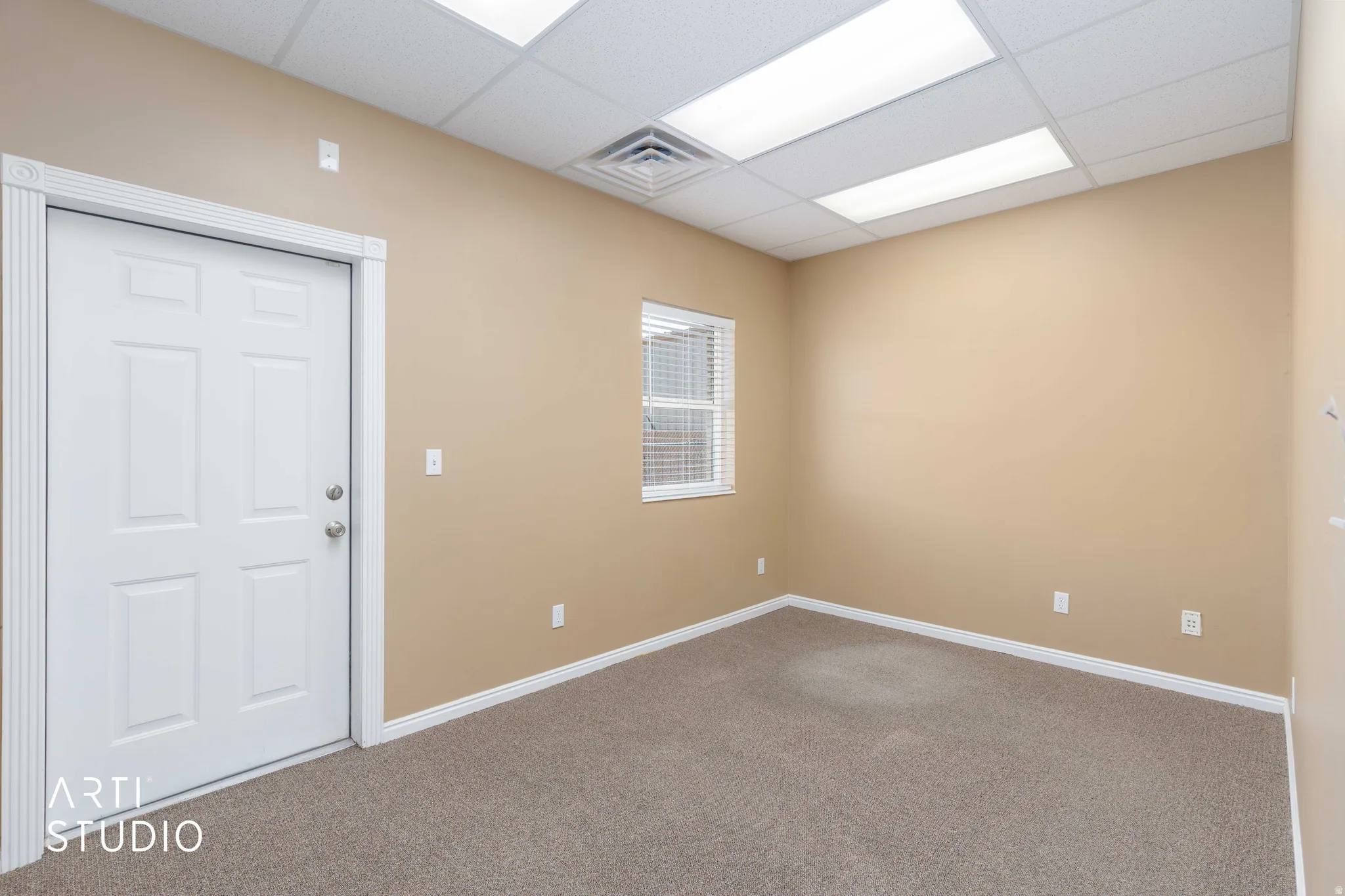 Neutral-toned room featuring a white paneled door with decorative trim, a single window with horizontal blinds, and textured carpet flooring