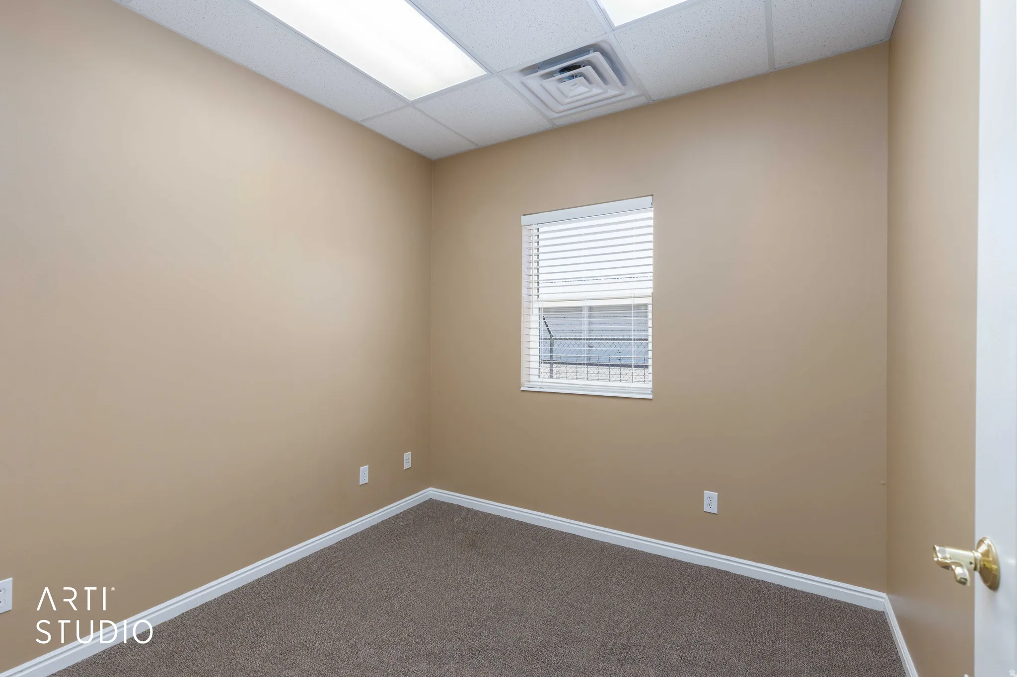 Interior room featuring neutral-toned walls, textured carpeting, and a white-trimmed window with horizontal blinds