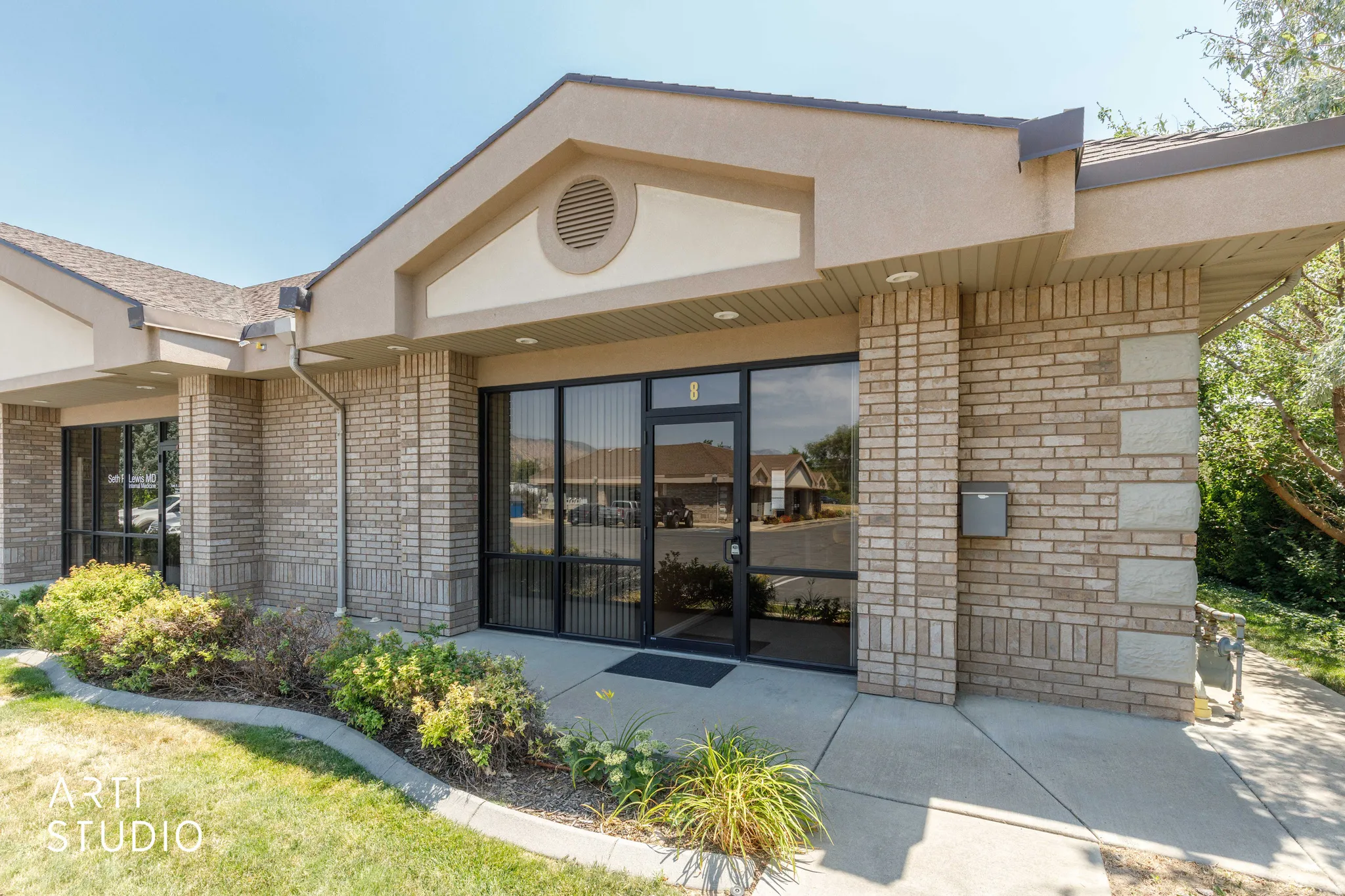 Brick and stucco exterior featuring multiple large windows, a central glass entry door, and a concrete walkway