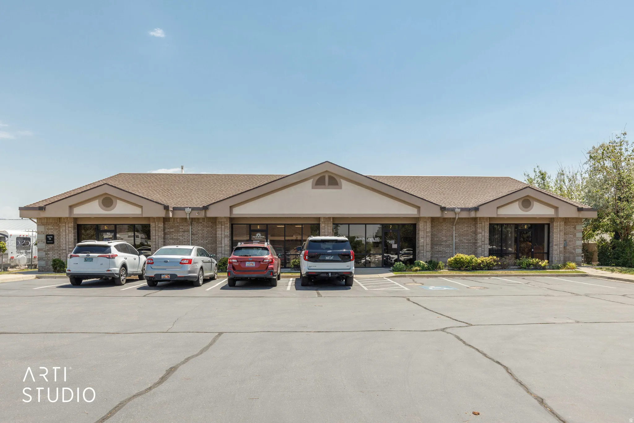 Commercial building featuring a brick facade, gabled roofline, multiple large storefront windows, and a paved parking lot with designated spaces