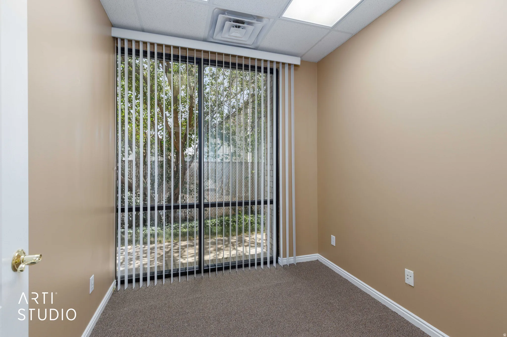 Interior room featuring large glass sliding doors with vertical blinds, textured carpet flooring, neutral painted walls, and white baseboards