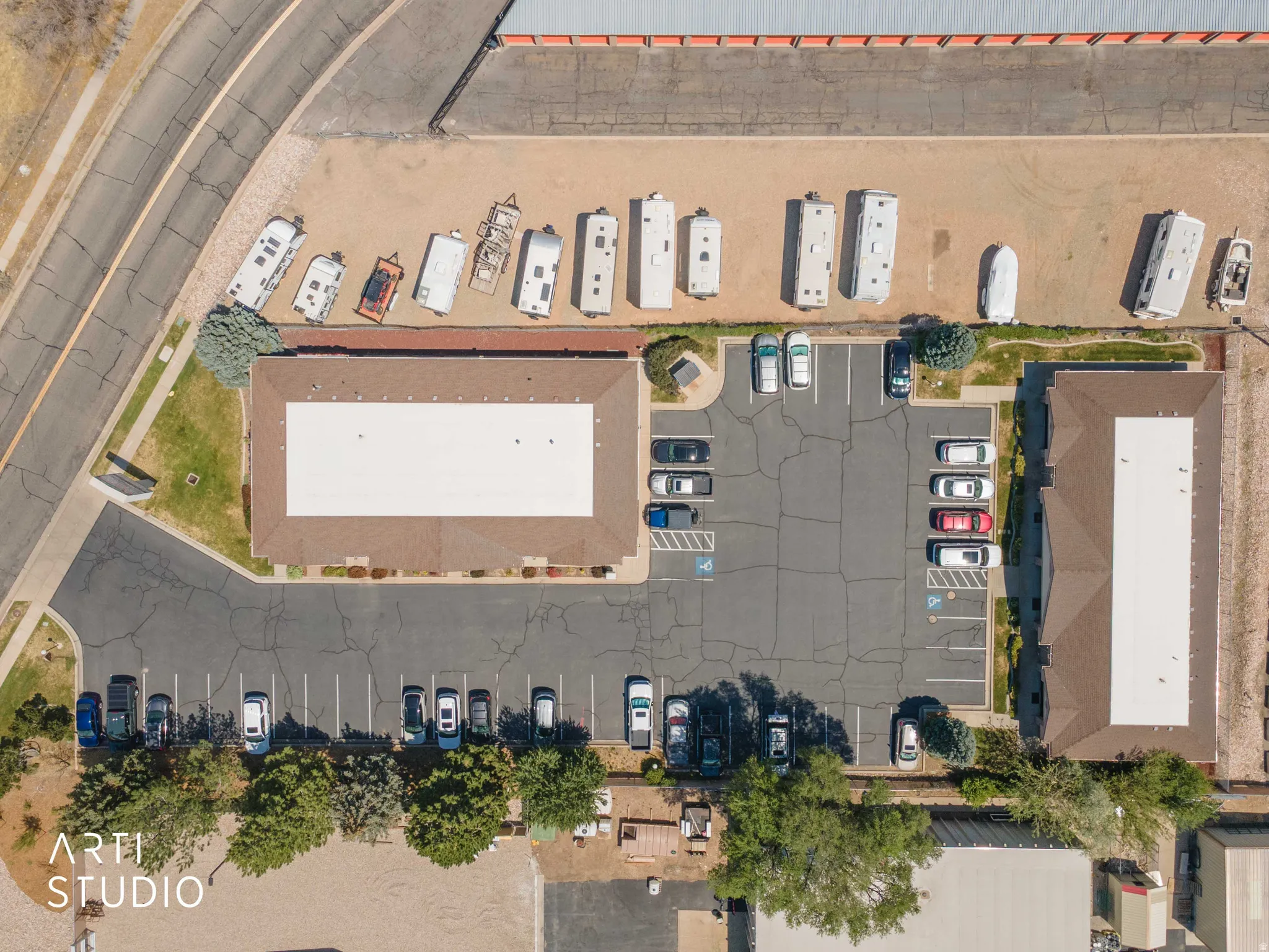 Aerial view showcasing two commercial buildings with brown roofs, extensive paved parking areas, and adjacent storage for recreational vehicles