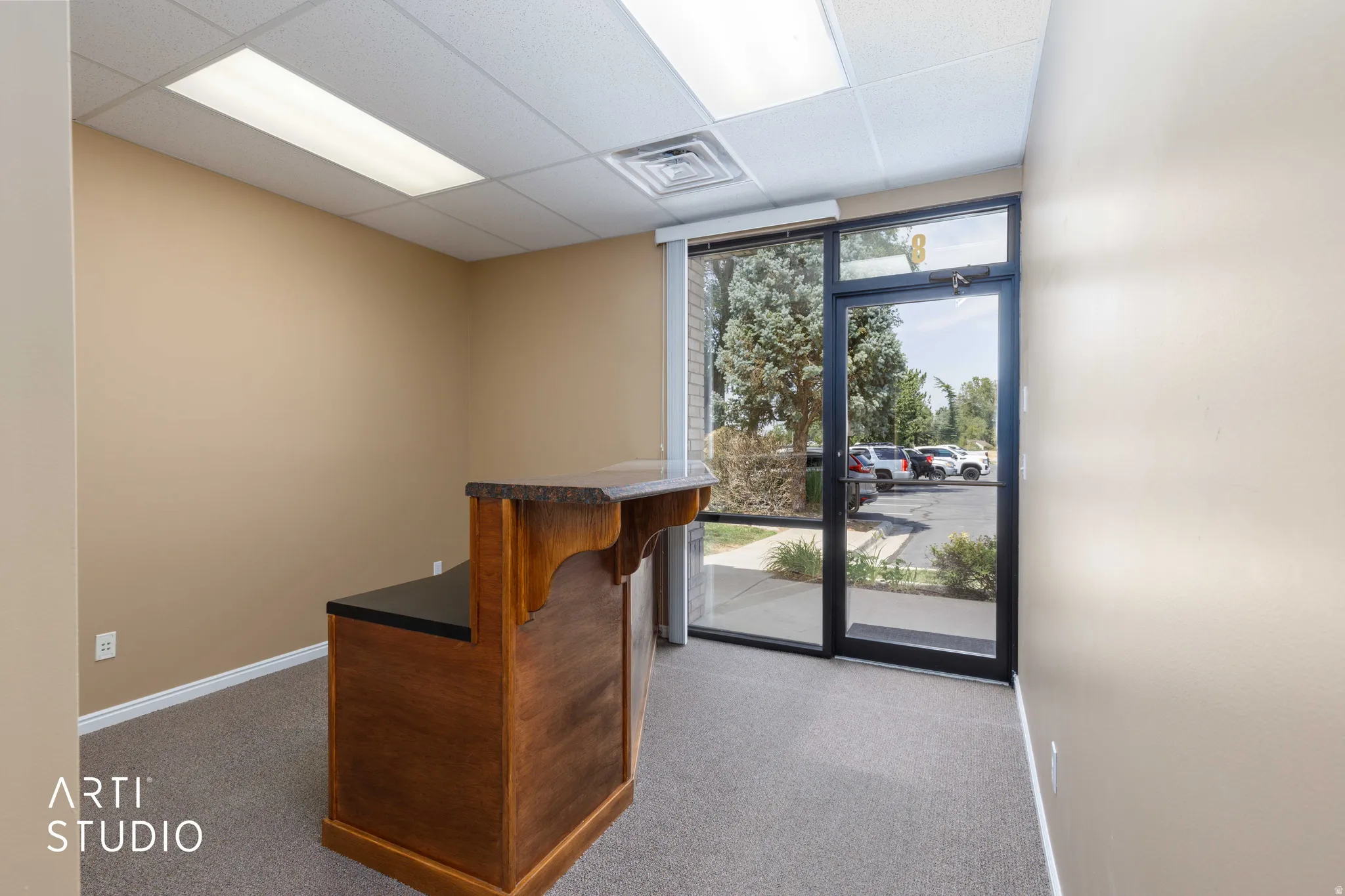 Entry area featuring a built-in wood-finish reception desk with a dark countertop, commercial-grade carpet, drop ceiling with recessed lighting, and a glass-paneled entry door with sidelight