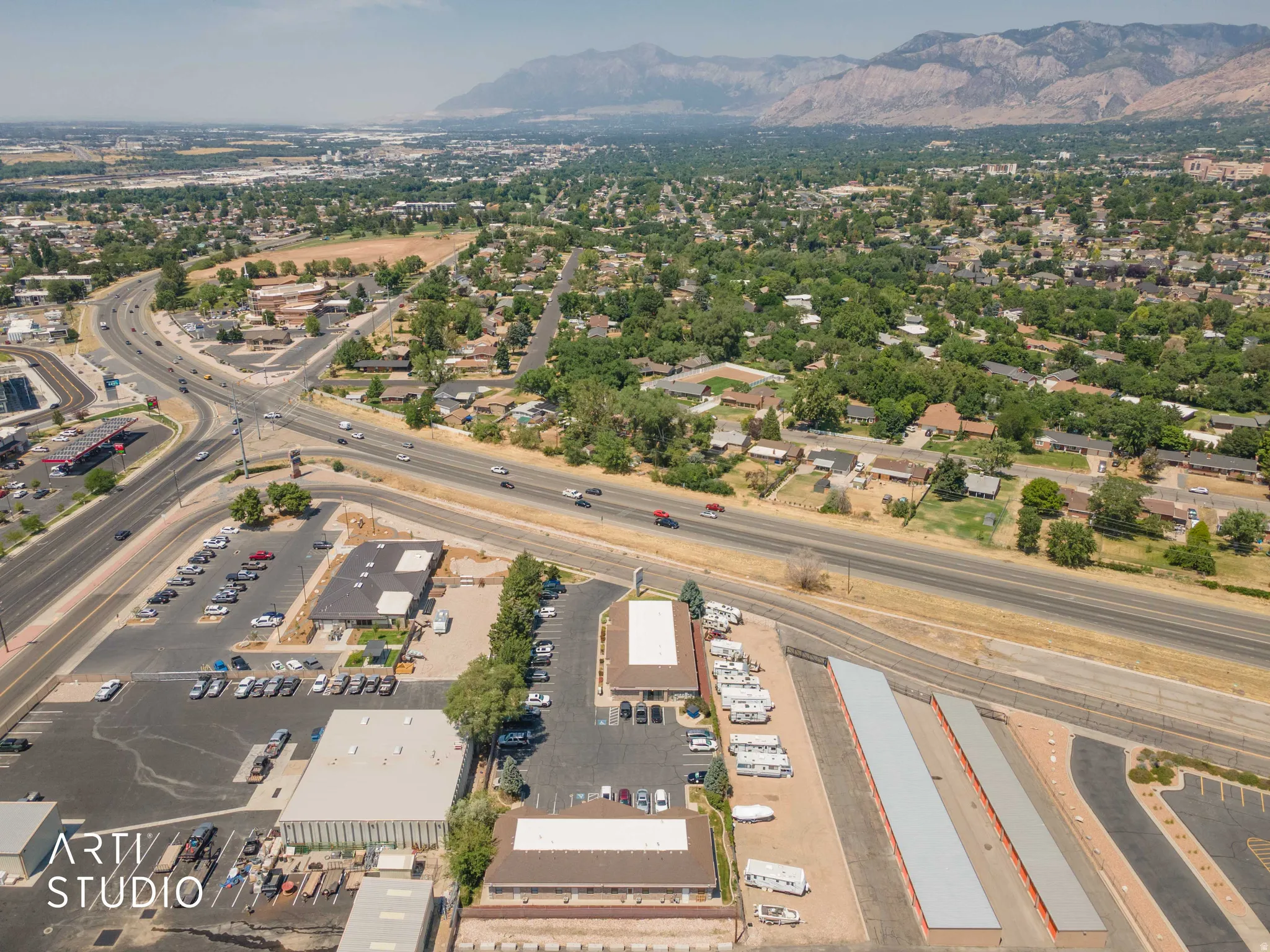 Aerial perspective showcasing commercial properties with extensive paved parking areas, highway access, and distant mountain scenery