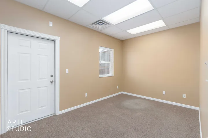 Neutral-toned room featuring a white paneled door with decorative trim, a single window with horizontal blinds, and textured carpet flooring