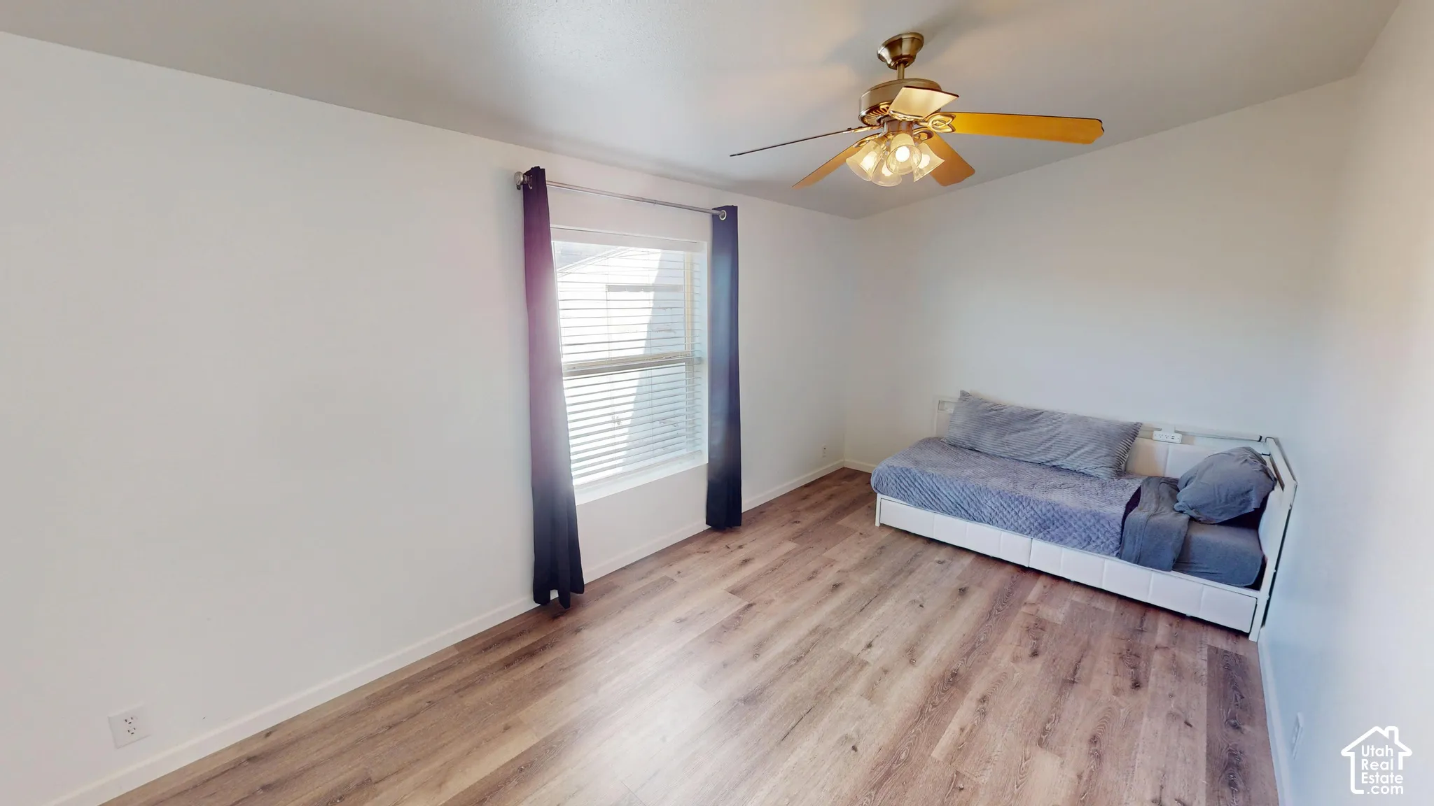 Spacious interior featuring wood-finish flooring, a ceiling fan with integrated lighting, a window with blinds, and white painted walls
