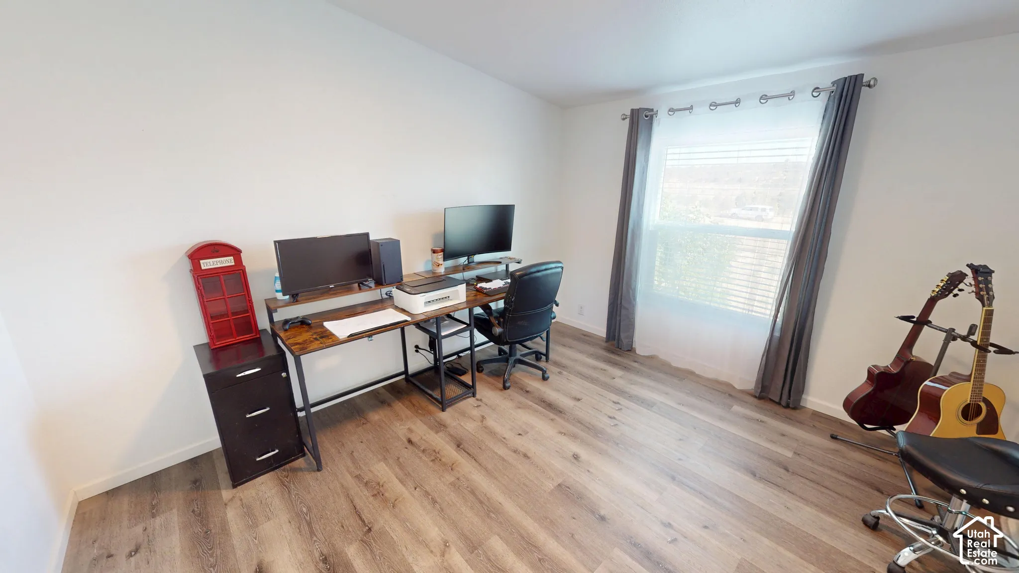 Room featuring light wood-finish flooring, white painted walls, and a large window with white blinds and grey drapes