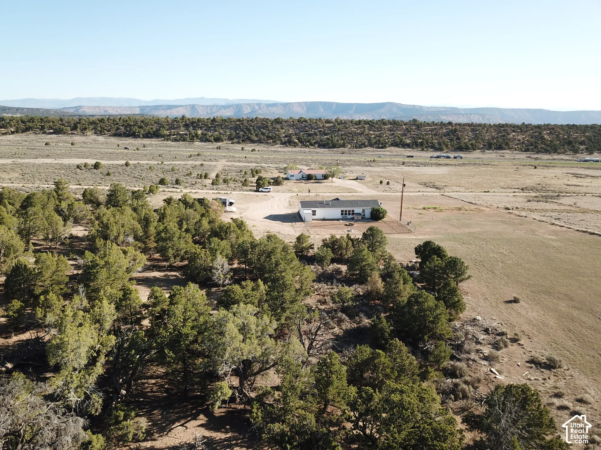 Expansive property featuring a white single-story residence, a broad unpaved driveway, and surrounding natural terrain