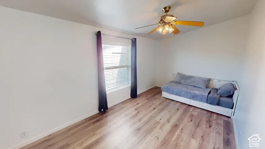 Spacious interior featuring wood-finish flooring, a ceiling fan with integrated lighting, a window with blinds, and white painted walls