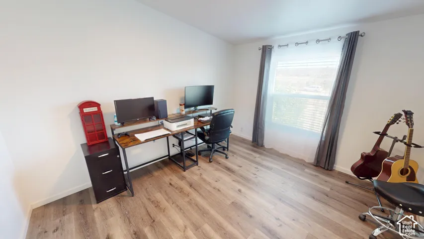 Room featuring light wood-finish flooring, white painted walls, and a large window with white blinds and grey drapes