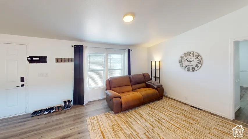 Bright living space featuring wood-finish flooring, white walls, and a large window with white blinds