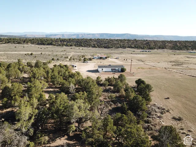Expansive property featuring a white single-story residence, a broad unpaved driveway, and surrounding natural terrain