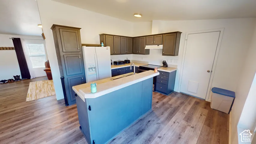 Kitchen featuring wood-finish flooring, dark cabinetry, light countertops, and a built-in breakfast bar