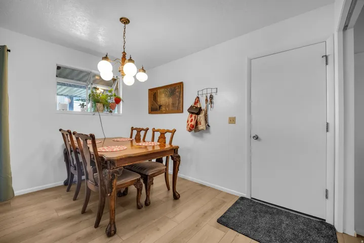 Bright dining space featuring a window, wood-finish flooring, white walls, and a five-light chandelier