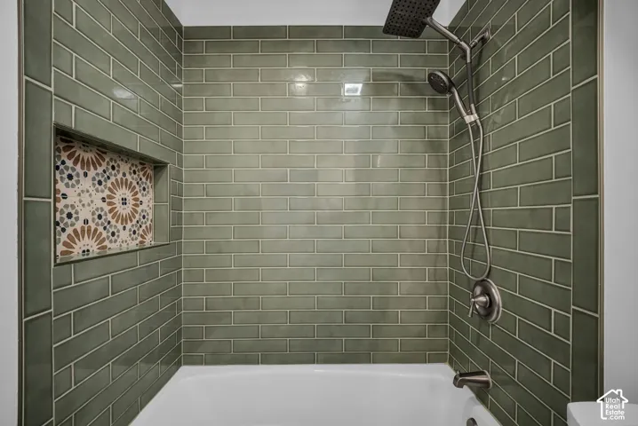 Bathroom featuring a dark gray vanity with a white countertop and integrated sink, wood-finish flooring, a white bathtub with green subway tile surround, and a rectangular mirror with a metal-finish fixture