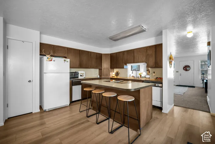 Open-concept kitchen featuring wood-finish flooring, dark wood cabinetry, light countertops, and a central island with seating
