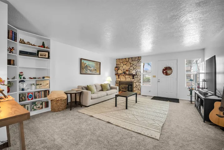 Living area featuring a stone-clad fireplace, built-in shelving, carpet flooring, a white entry door, and multiple windows