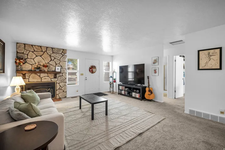 Living area featuring a stone-clad fireplace with a wood mantel, light-colored carpeting, white walls, a white entry door, and a built-in entertainment stand