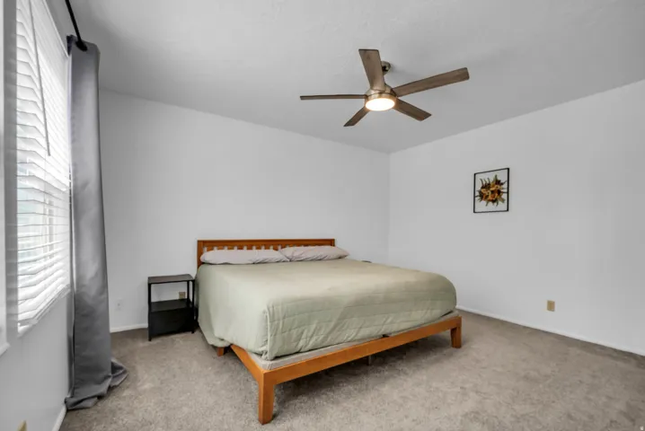 Bedroom featuring light gray carpet flooring, a ceiling fan with integrated lighting, and a window with horizontal blinds