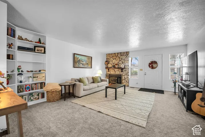 Living area featuring a stone-clad fireplace, built-in shelving, carpet flooring, a white entry door, and multiple windows