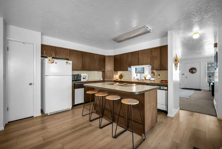 Open-concept kitchen featuring wood-finish flooring, dark wood cabinetry, light countertops, and a central island with seating