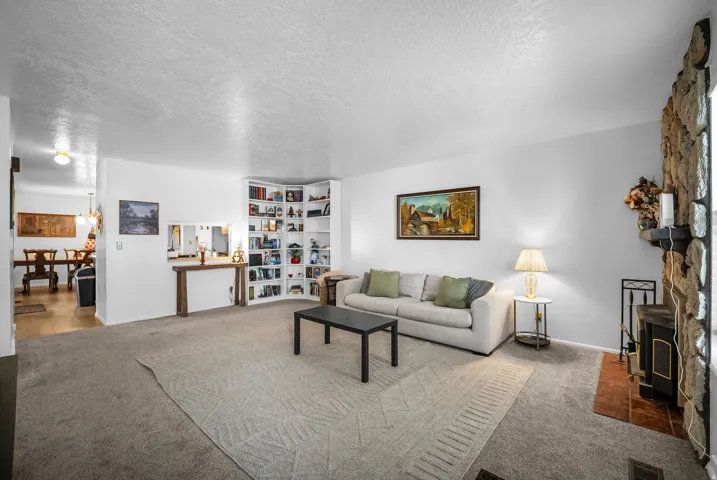 Spacious living area featuring carpet flooring, a stone-clad fireplace with a hearth, and built-in corner shelving