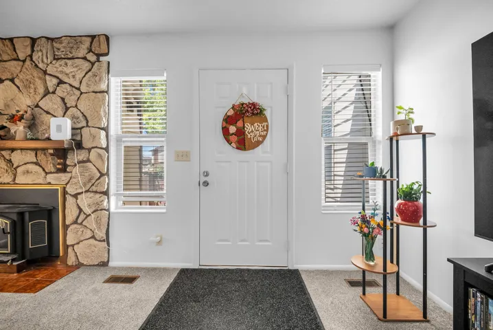 Entryway featuring a stone-clad fireplace with wood mantle, white paneled door, and two side windows with blinds