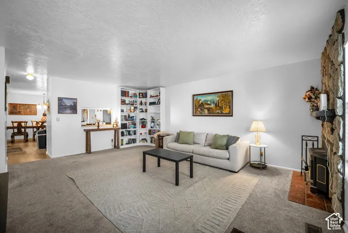 Spacious living area featuring carpet flooring, a stone-clad fireplace with a hearth, and built-in corner shelving