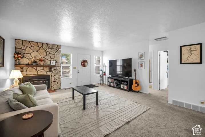 Living area featuring a stone-clad fireplace with a wood mantel, light-colored carpeting, white walls, a white entry door, and a built-in entertainment stand