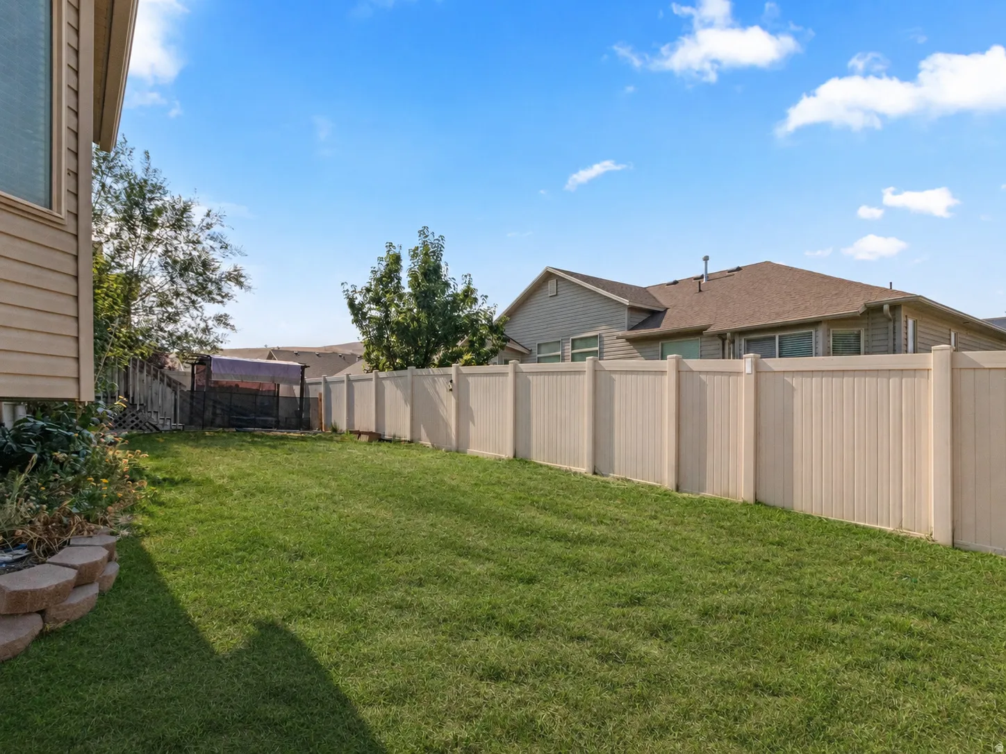 Expansive fenced backyard featuring a manicured lawn, a retaining wall with stacked stone, and a tan vinyl privacy fence