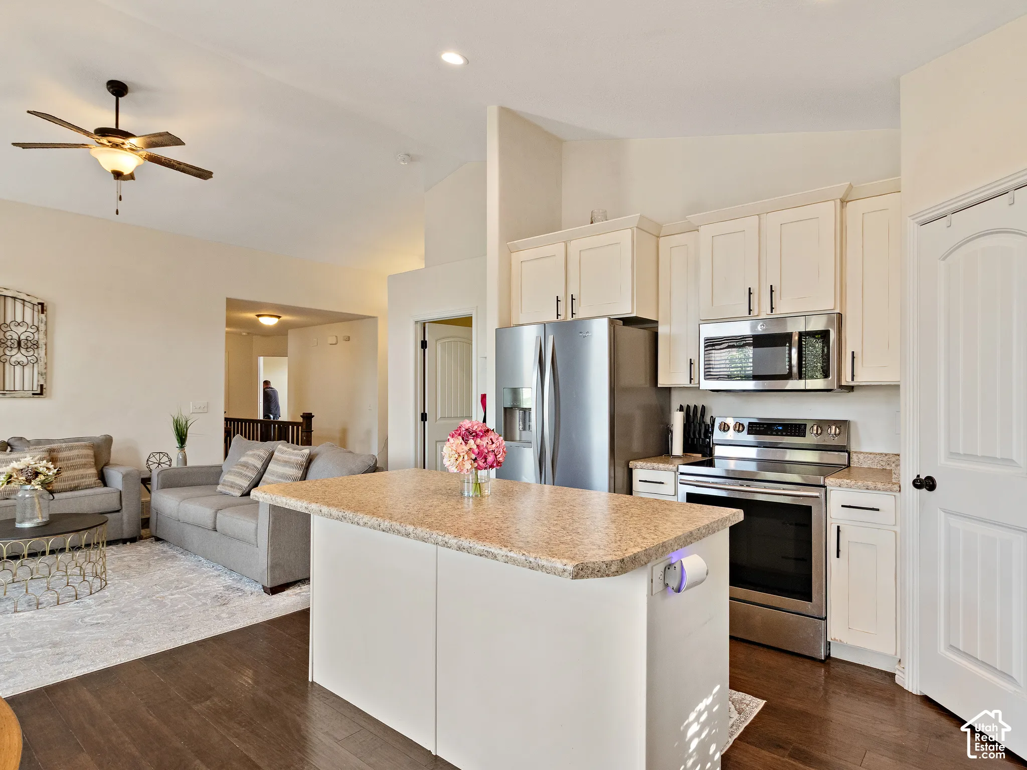 Kitchen island featuring a light-toned countertop, white cabinetry, stainless steel appliances, dark wood-finish flooring, and recessed lighting