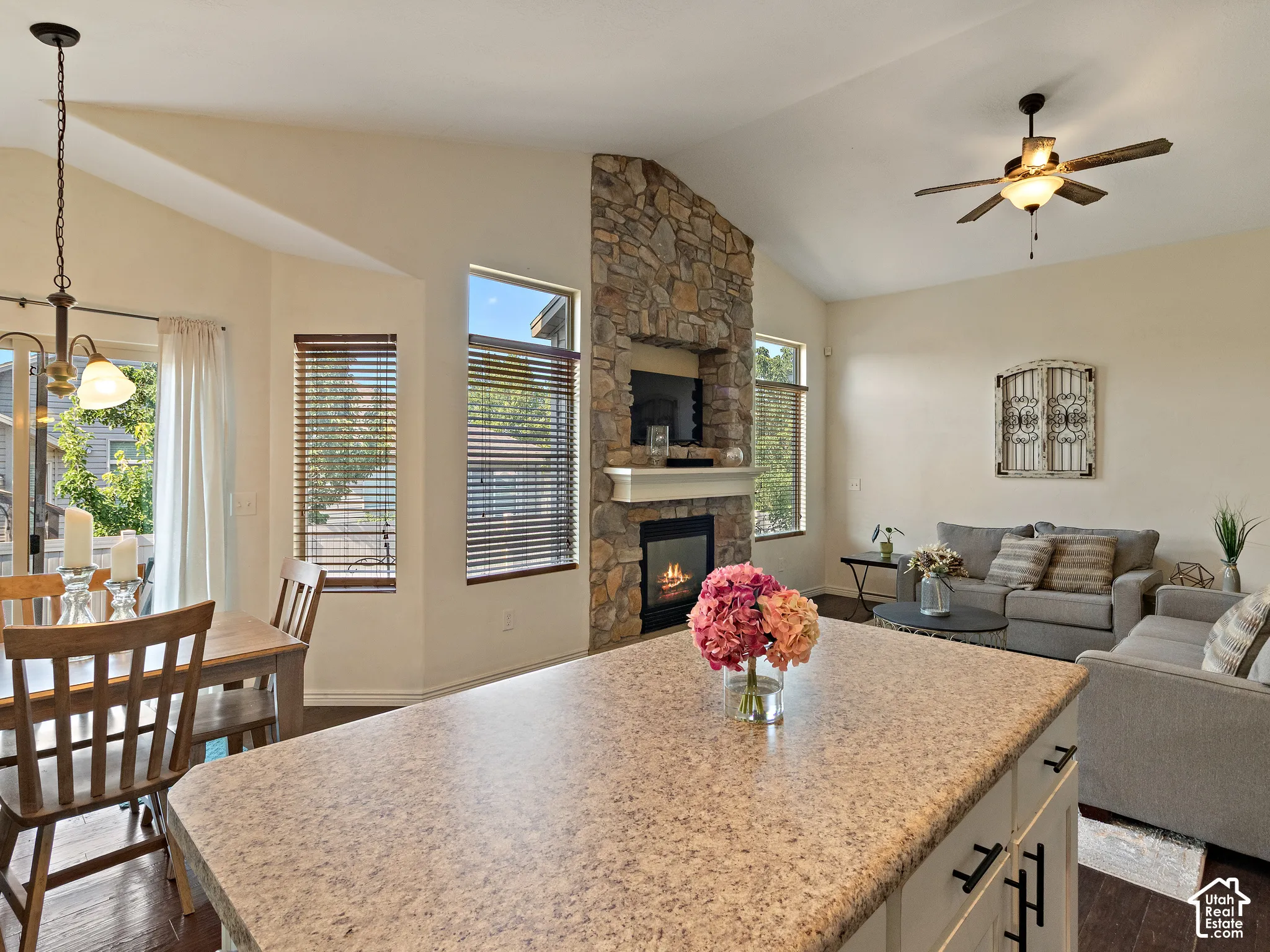 Open-concept living space featuring vaulted ceilings, a stone-clad fireplace with a hearth, dark wood-finish flooring, and a dining area with a glass-paned door