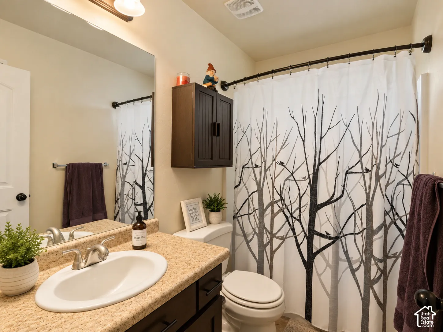 Vanity with a neutral-toned countertop and an integrated sink, dark wood-finish cabinetry, a full-width wall mirror, and an overhead light fixture