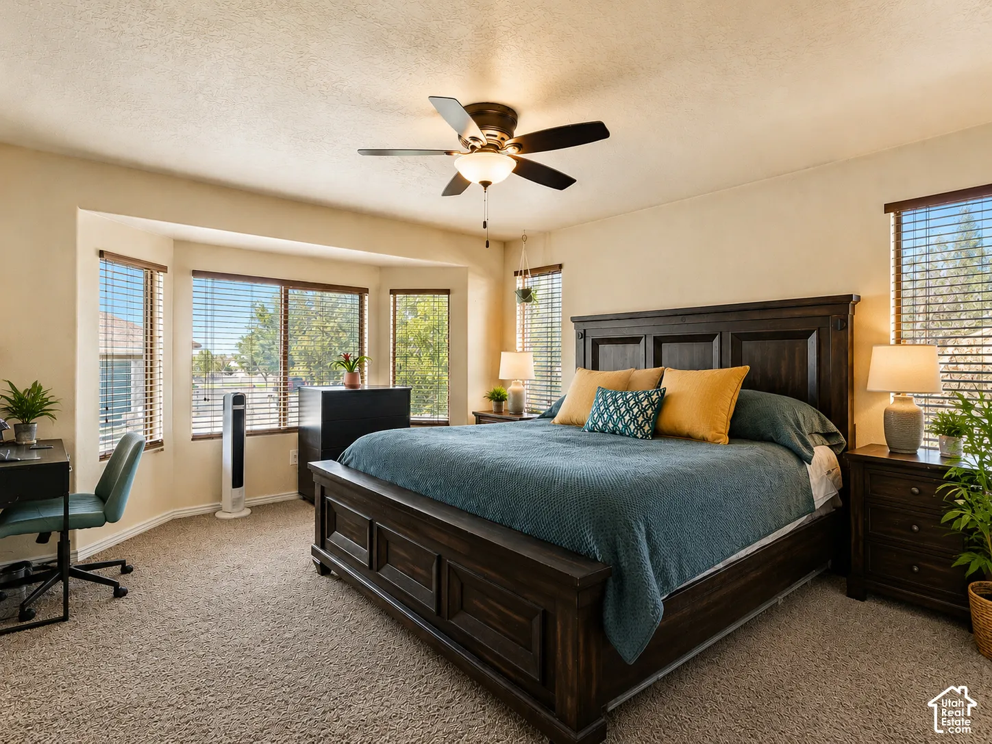 Expansive bedroom featuring carpet flooring, a bay window with blinds, and a ceiling fan with integrated lighting