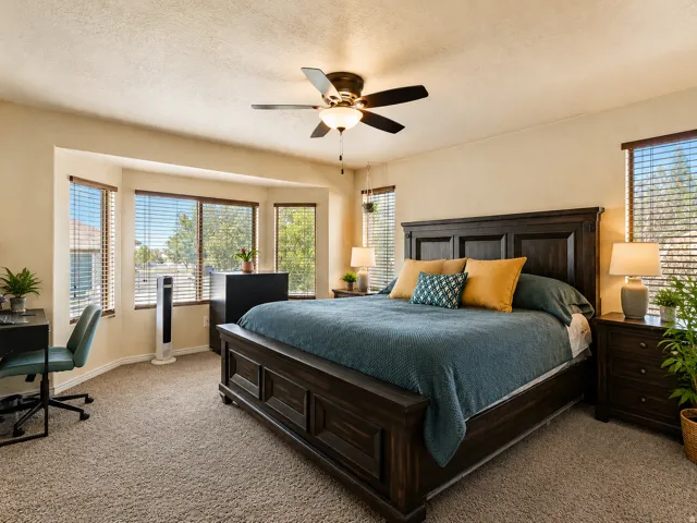 Expansive bedroom featuring carpet flooring, a bay window with blinds, and a ceiling fan with integrated lighting