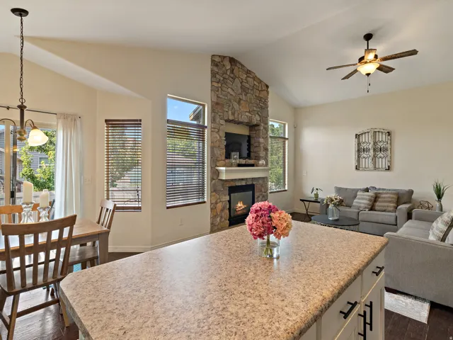 Open-concept living space featuring vaulted ceilings, a stone-clad fireplace with a hearth, dark wood-finish flooring, and a dining area with a glass-paned door
