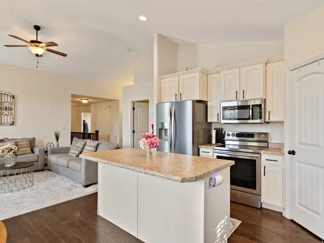 Kitchen island featuring a light-toned countertop, white cabinetry, stainless steel appliances, dark wood-finish flooring, and recessed lighting