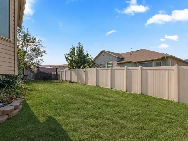 Expansive fenced backyard featuring a manicured lawn, a retaining wall with stacked stone, and a tan vinyl privacy fence