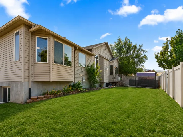 Expansive green lawn defines the backyard, bordered by a white privacy fence